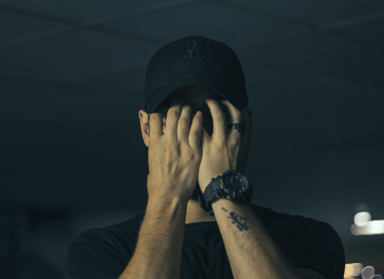 a frustrated man in a baseball hat covering his face